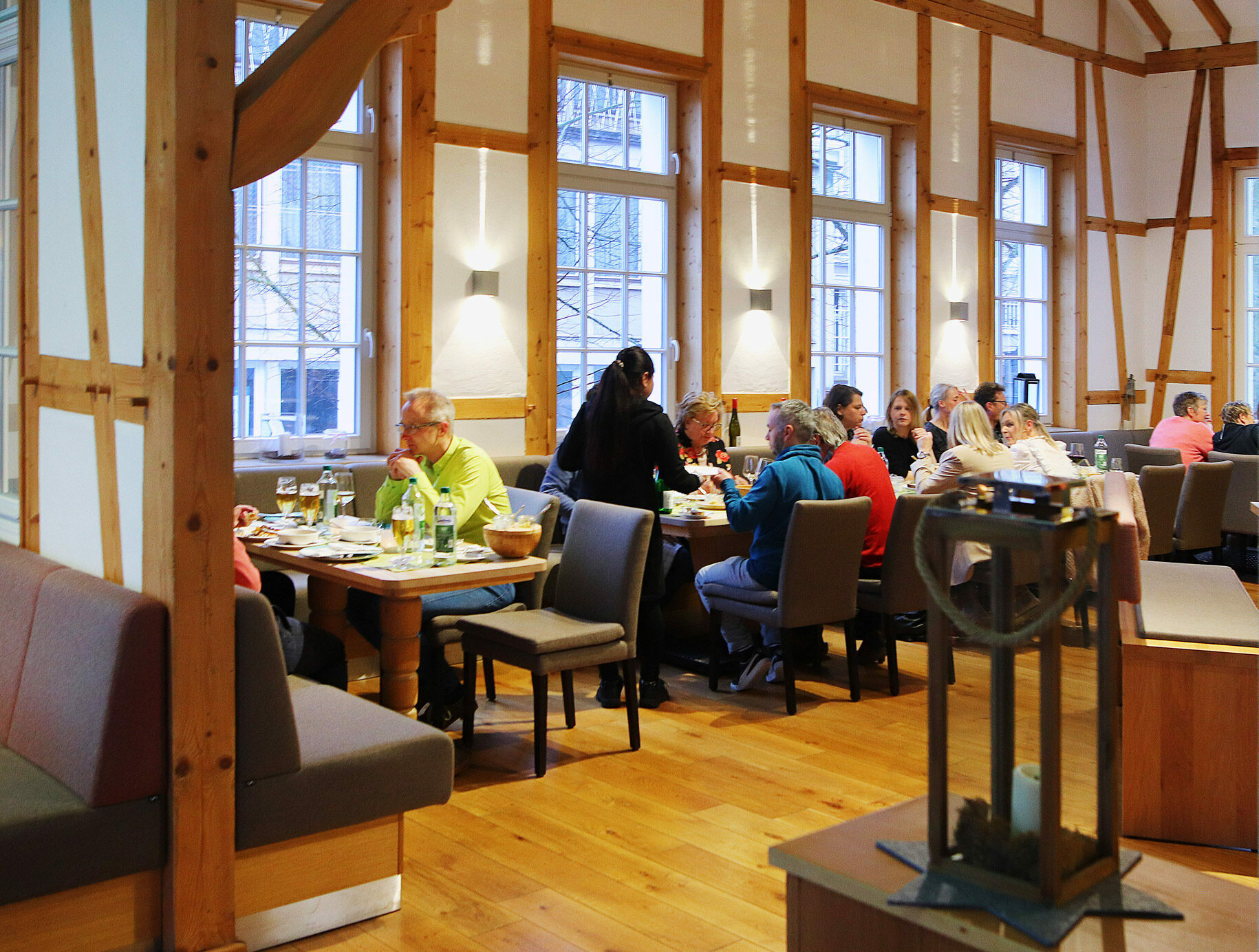 Ein gemütliches Restaurant mit Holzbalken und weißen Wänden, mit einem langen Holztisch, grauen Stühlen und einem warmen Ambiente, in dem die Gäste sitzen und ihre Mahlzeiten genießen.